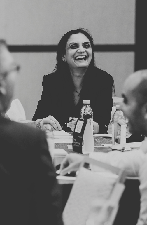 Black and white photo of a woman smiling and engaged in a lively discussion around a conference table with colleagues and bottled water Black and white photo of a woman smiling and engaged in a lively discussion around a conference table with colleagues and bottled water